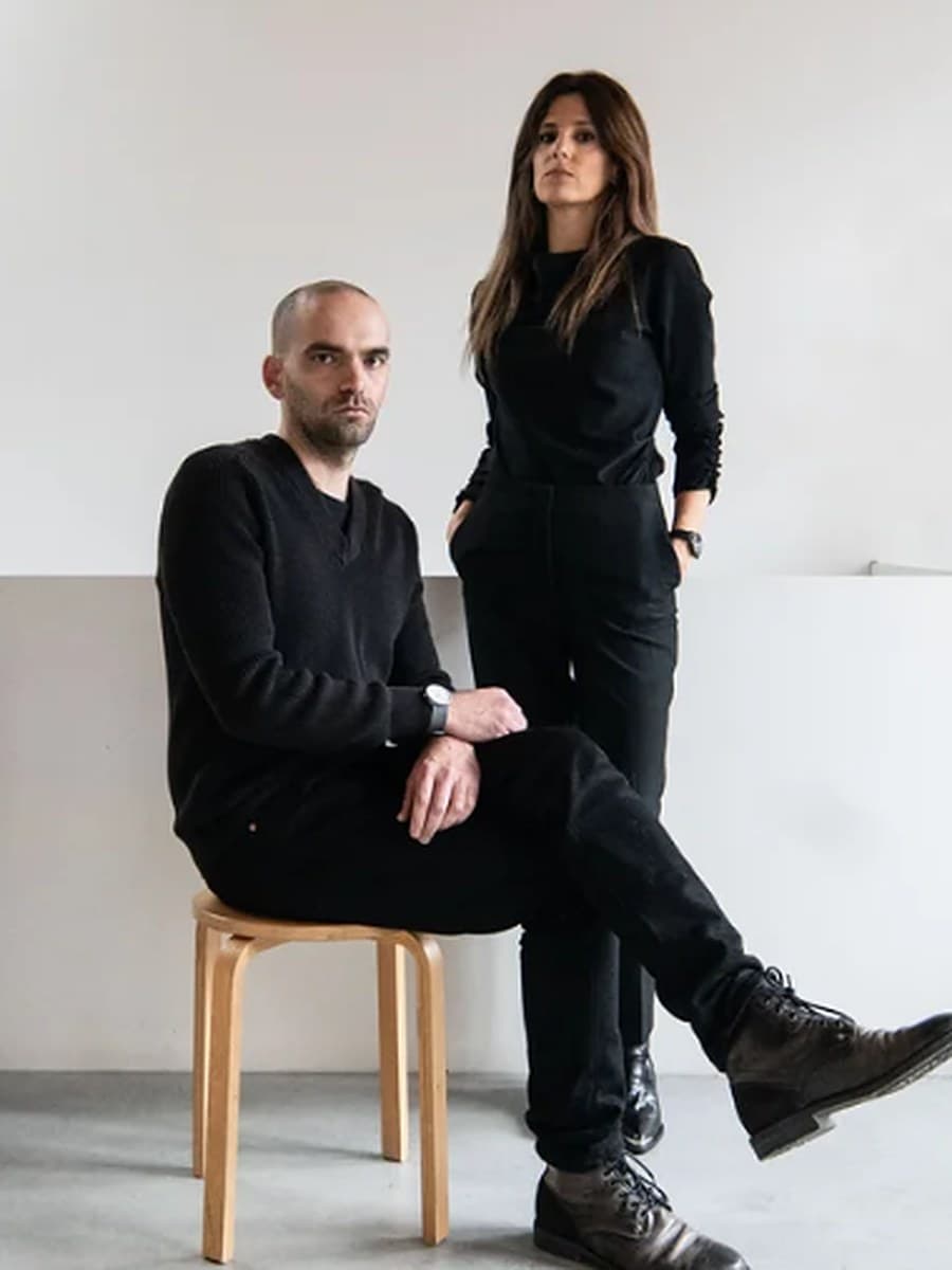 The Gabinete Antifrágil team in a pale studio: the architect João Franco seated on a stool and a colleague standing beside him, both dressed in black.
